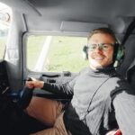 pilot wearing glasses in a cockpit of a plane on a field.
