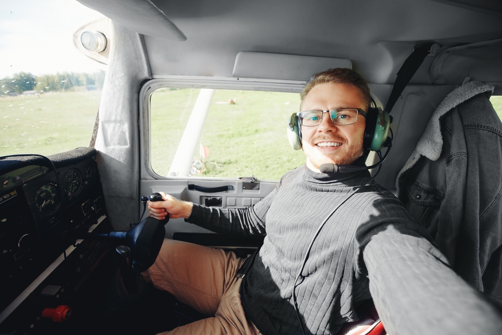 pilot wearing glasses in a cockpit of a plane on a field.