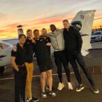Image of flight school students next to a Cessna as the sun is setting on the runway