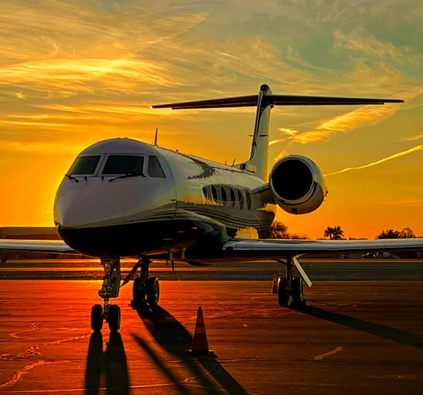 Image of a commercial jet on a runway with the sunset behind it.